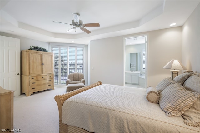 bedroom with ceiling fan, a raised ceiling, light carpet, and ensuite bath