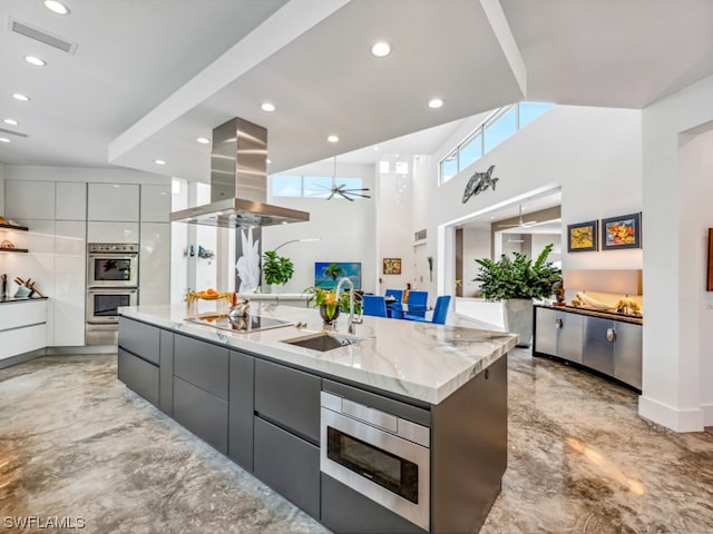 kitchen with sink, stainless steel appliances, light stone counters, a spacious island, and island range hood