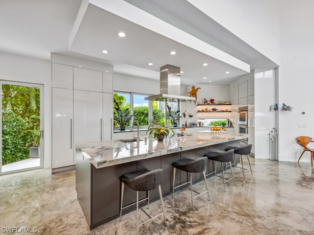 kitchen featuring gray cabinetry, light stone countertops, a large island, island range hood, and a breakfast bar