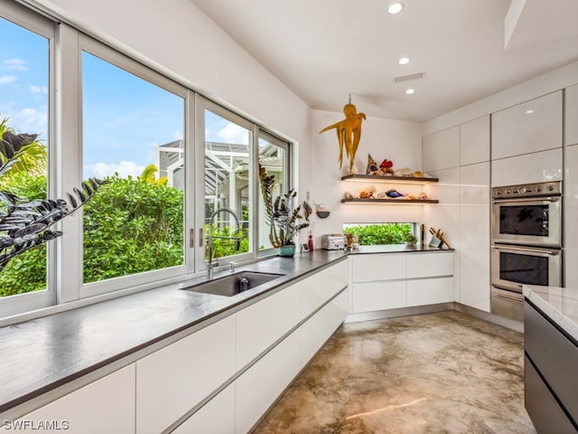 kitchen featuring white cabinets, stainless steel double oven, plenty of natural light, and sink