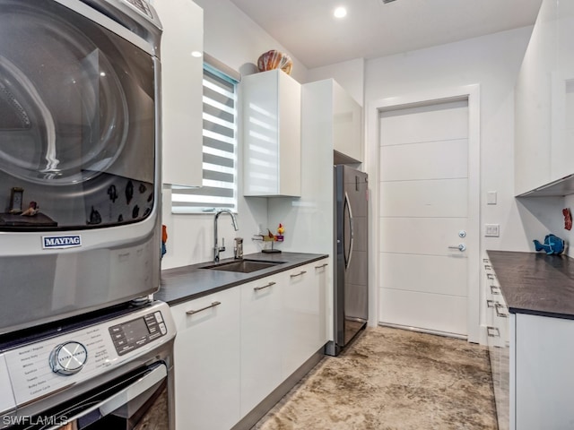 kitchen featuring stainless steel refrigerator, white cabinetry, stacked washer and dryer, and sink