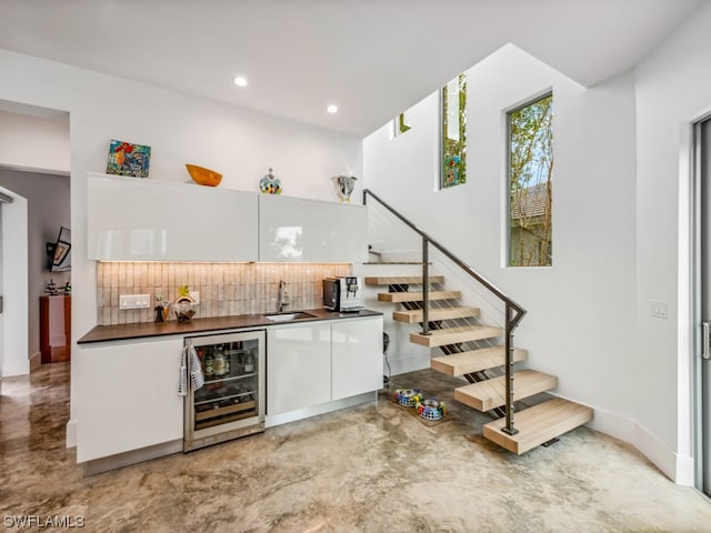 bar featuring sink, white cabinetry, backsplash, and beverage cooler