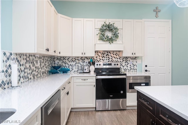 kitchen with light wood-type flooring, appliances with stainless steel finishes, white cabinets, light stone countertops, and backsplash