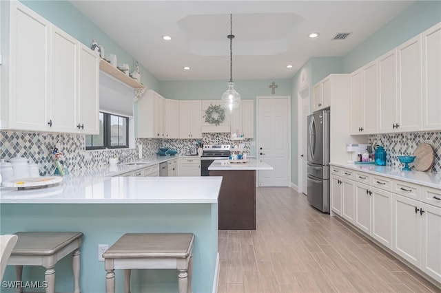 kitchen with appliances with stainless steel finishes, white cabinetry, hanging light fixtures, a kitchen bar, and kitchen peninsula