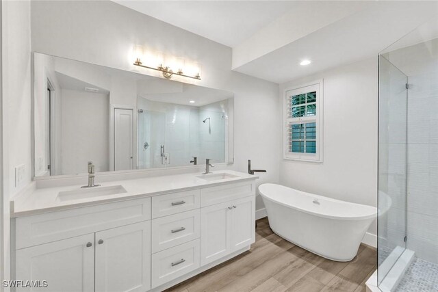 bathroom with a stall shower, double vanity, a sink, and wood finished floors