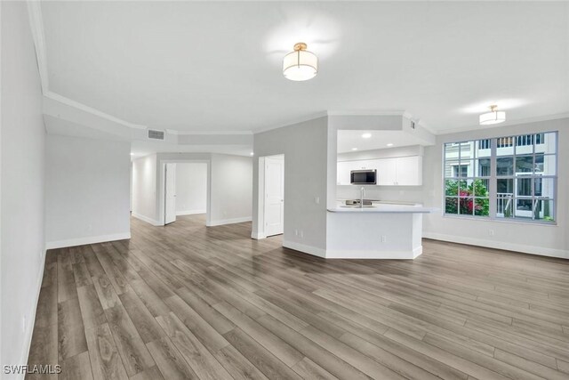 unfurnished living room featuring a sink, wood finished floors, visible vents, baseboards, and ornamental molding