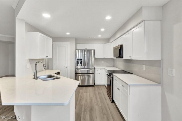 kitchen with stainless steel appliances, a peninsula, a sink, light countertops, and light wood-type flooring