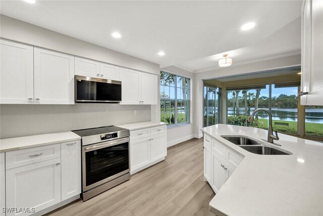 kitchen with white cabinets, appliances with stainless steel finishes, light countertops, crown molding, and a sink