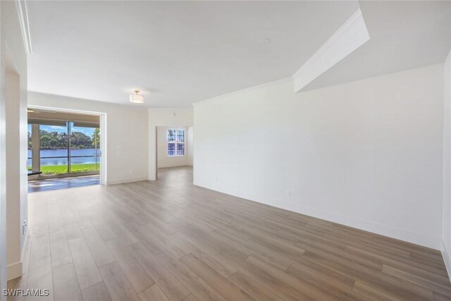 spare room featuring a water view, crown molding, baseboards, and wood finished floors