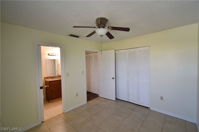 unfurnished bedroom featuring ceiling fan, ensuite bath, a textured ceiling, light tile floors, and sink