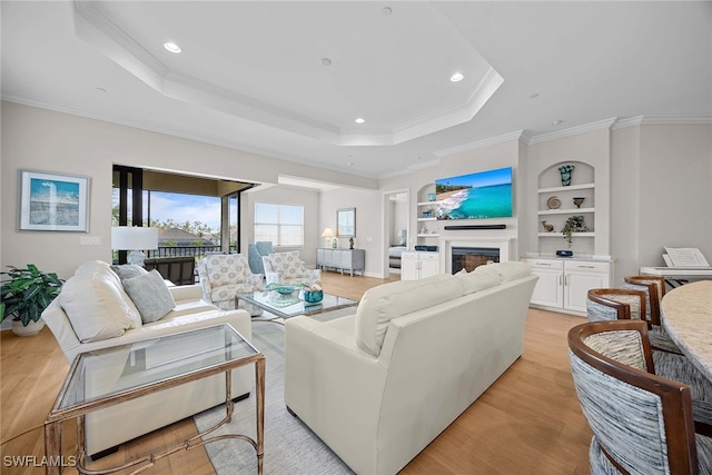 living room with crown molding, light hardwood / wood-style flooring, built in features, and a raised ceiling