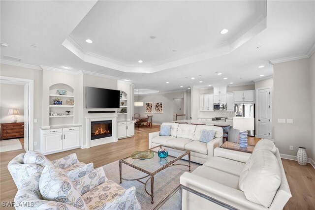 living room with light hardwood / wood-style flooring, ornamental molding, and a tray ceiling