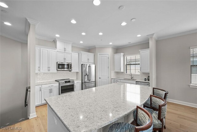 kitchen with white cabinets, a kitchen breakfast bar, light hardwood / wood-style flooring, stainless steel appliances, and a center island