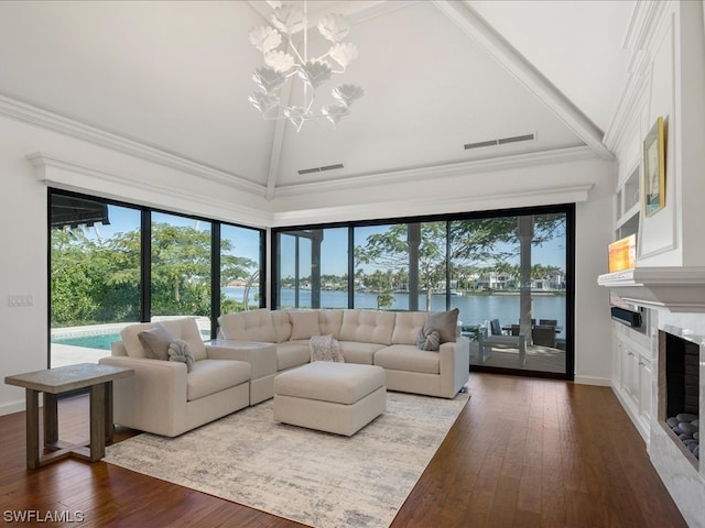 living room featuring vaulted ceiling, a healthy amount of sunlight, a water view, an inviting chandelier, and a fireplace