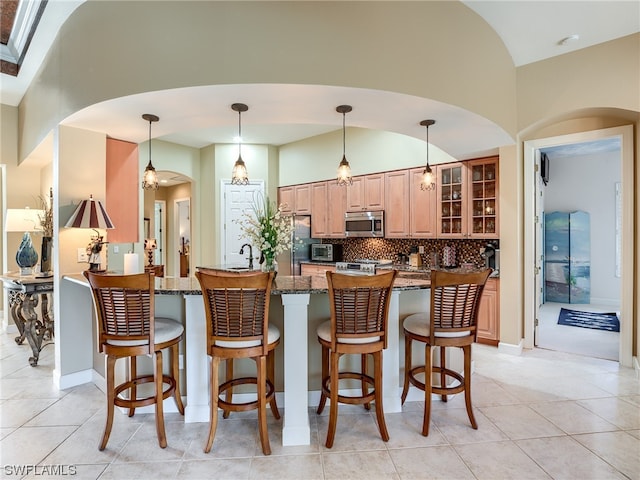 kitchen featuring a kitchen bar, stainless steel appliances, light tile floors, dark stone counters, and tasteful backsplash