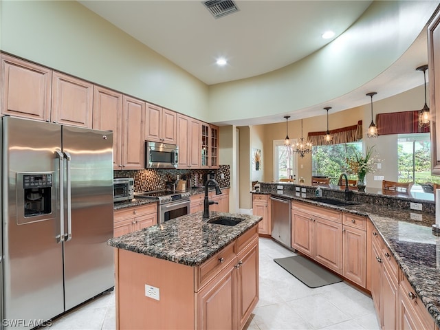 kitchen with sink, dark stone counters, high end appliances, a center island with sink, and decorative light fixtures