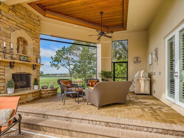 sunroom with an outdoor stone fireplace, a raised ceiling, ceiling fan, and wood ceiling