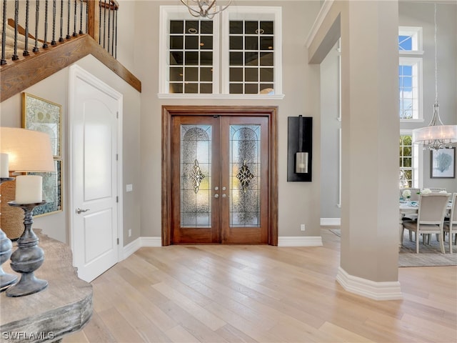 entryway with light hardwood / wood-style flooring, a towering ceiling, an inviting chandelier, and french doors