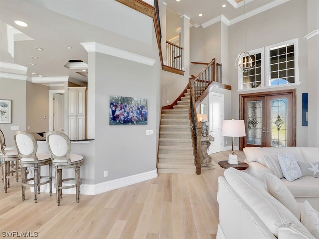 foyer entrance featuring a high ceiling, light hardwood / wood-style flooring, french doors, ornamental molding, and a chandelier