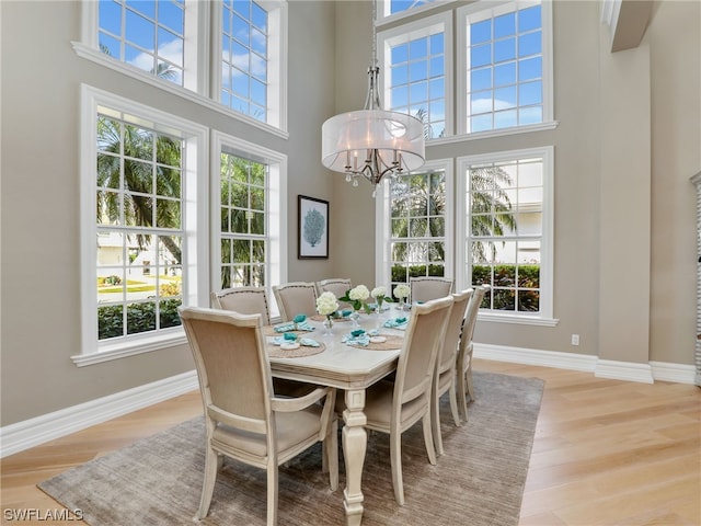 dining room featuring light wood-type flooring, a towering ceiling, and a healthy amount of sunlight