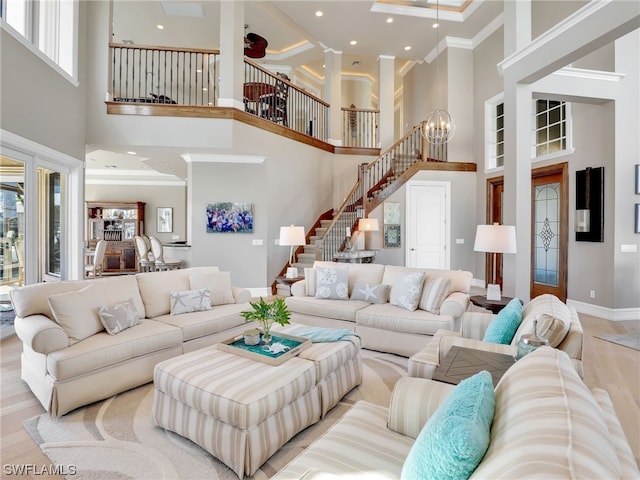 living room featuring a towering ceiling, light wood-type flooring, and crown molding