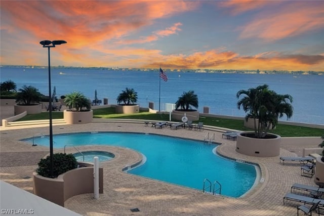 pool at dusk featuring a patio area, a water view, and a community hot tub