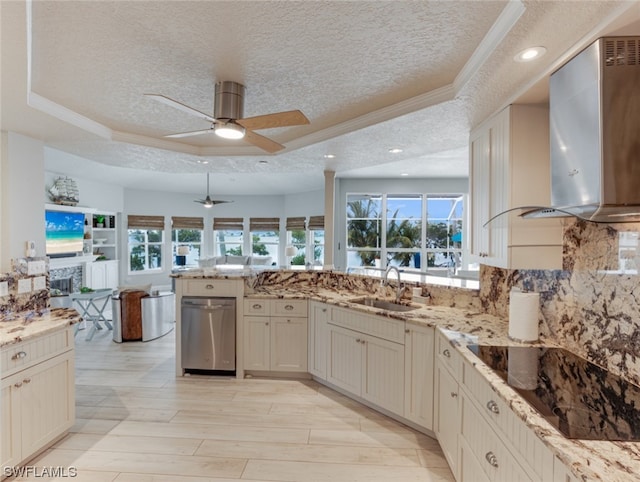 kitchen featuring a tray ceiling, light stone counters, sink, and wall chimney range hood