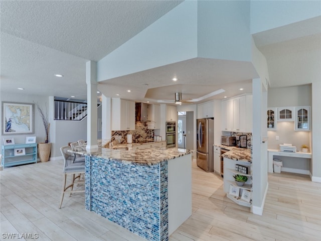 kitchen with a raised ceiling, white cabinets, appliances with stainless steel finishes, backsplash, and light stone countertops