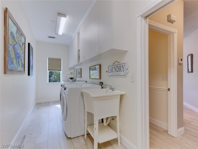 laundry area with washing machine and dryer, cabinets, and light wood-type flooring