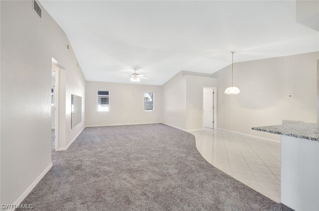 empty room with vaulted ceiling, light tile floors, and ceiling fan with notable chandelier