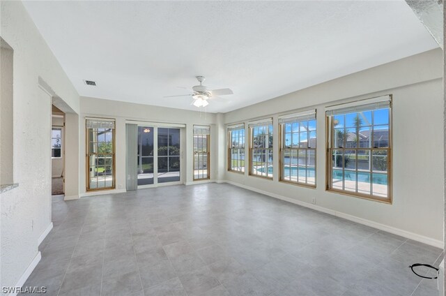 empty room with light tile floors, ceiling fan, and a wealth of natural light