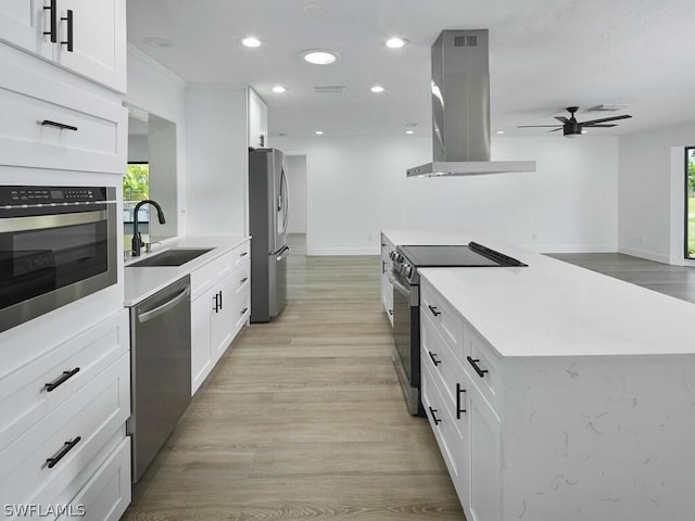 kitchen with sink, appliances with stainless steel finishes, island range hood, white cabinets, and light wood-type flooring