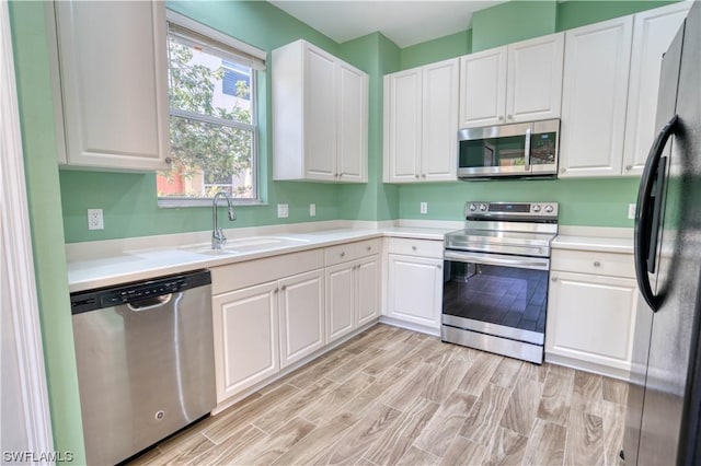 kitchen with stainless steel appliances, sink, white cabinets, and light hardwood / wood-style floors