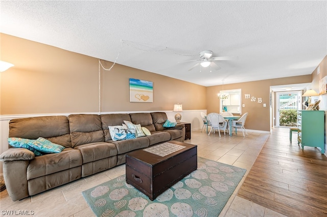 living room with a textured ceiling, ceiling fan with notable chandelier, and light wood-type flooring