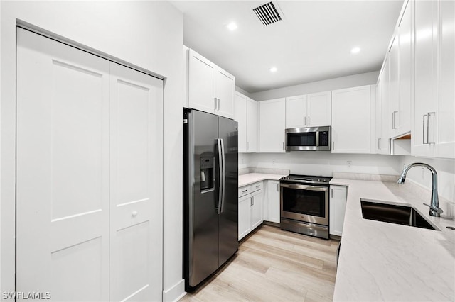 kitchen featuring light stone countertops, visible vents, a sink, stainless steel appliances, and light wood-style floors