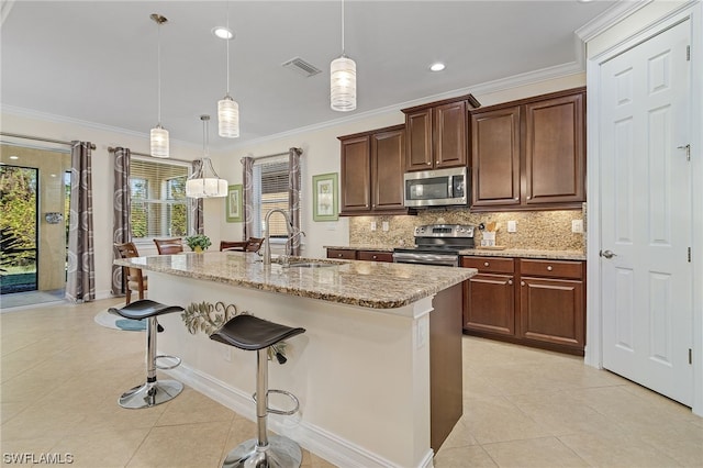 kitchen featuring a kitchen bar, sink, appliances with stainless steel finishes, pendant lighting, and a kitchen island with sink