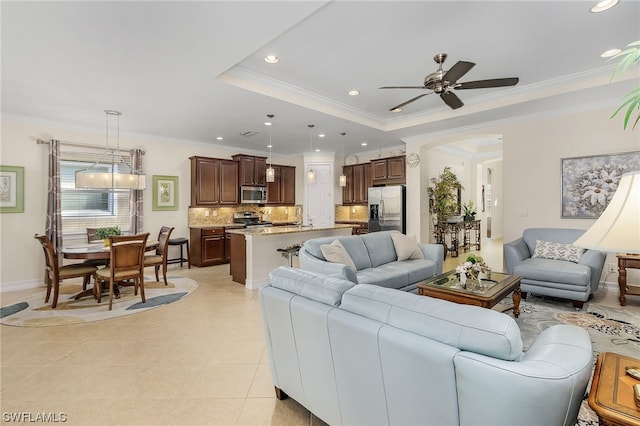 living room with ceiling fan, ornamental molding, a raised ceiling, and sink