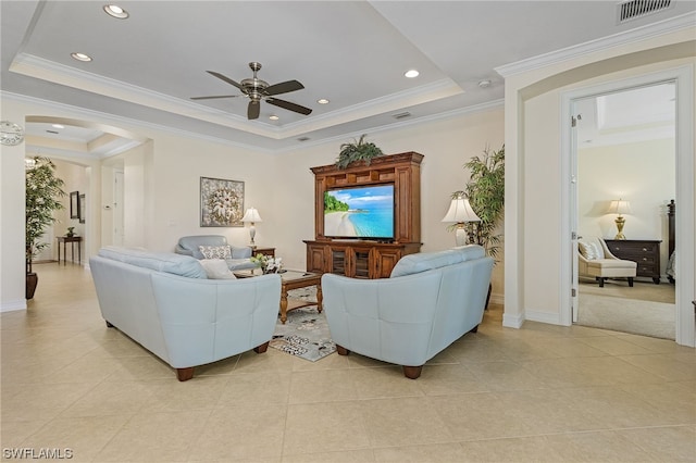 living room featuring ceiling fan, ornamental molding, a tray ceiling, and light tile patterned floors