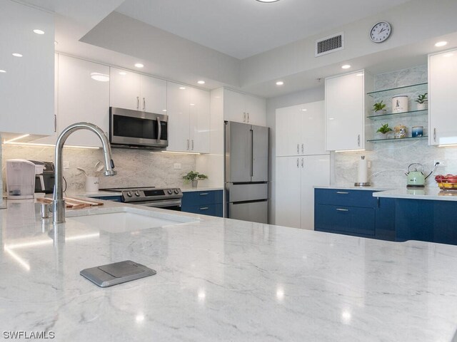 kitchen with blue cabinetry, stainless steel appliances, light stone countertops, sink, and white cabinets