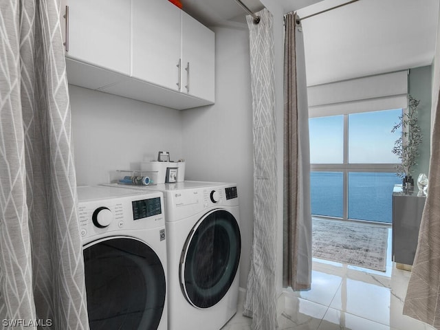 clothes washing area featuring washing machine and dryer, cabinets, and a water view