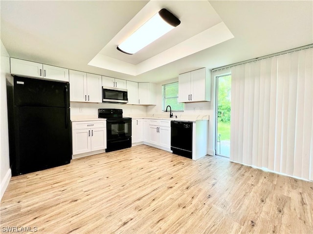 kitchen featuring a tray ceiling, white cabinetry, light hardwood / wood-style floors, and black appliances