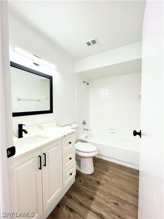 full bathroom with bathtub / shower combination, wood-type flooring, vanity, and toilet