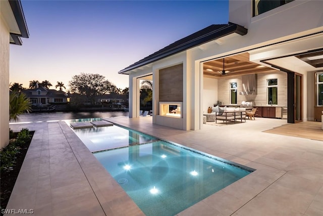 pool at dusk with outdoor lounge area, a water view, ceiling fan, an in ground hot tub, and a patio