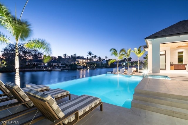 pool at dusk featuring a water view and a hot tub