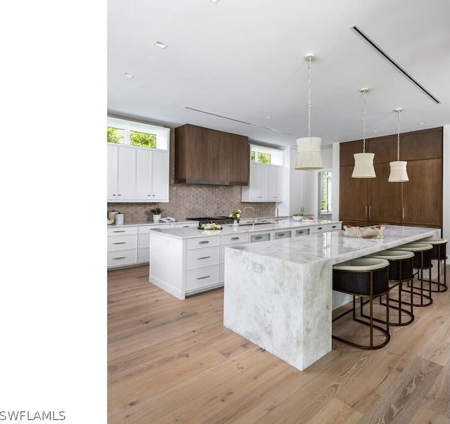 kitchen with a breakfast bar, white cabinets, a spacious island, light hardwood / wood-style floors, and dark brown cabinetry