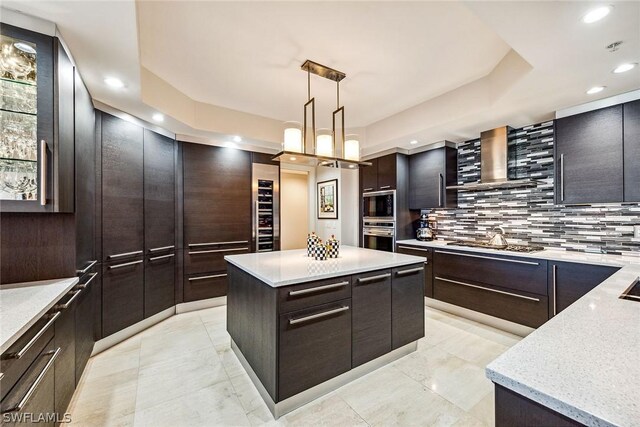 kitchen featuring hanging light fixtures, decorative backsplash, wall chimney exhaust hood, appliances with stainless steel finishes, and light tile patterned floors