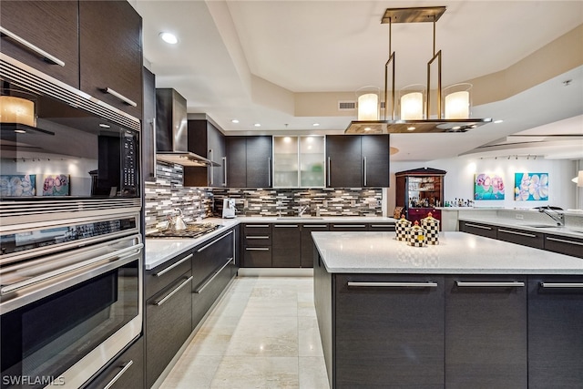 kitchen with light tile patterned flooring, wall chimney range hood, backsplash, a center island, and decorative light fixtures