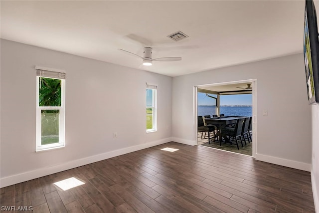 unfurnished room featuring dark wood-type flooring, ceiling fan, and a water view