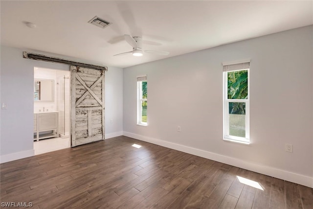 empty room with a barn door, ceiling fan, and dark hardwood / wood-style floors