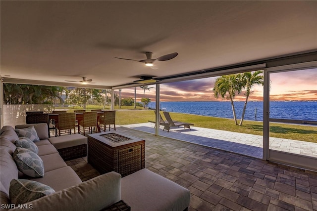 patio terrace at dusk featuring a water view, an outdoor hangout area, ceiling fan, and a yard